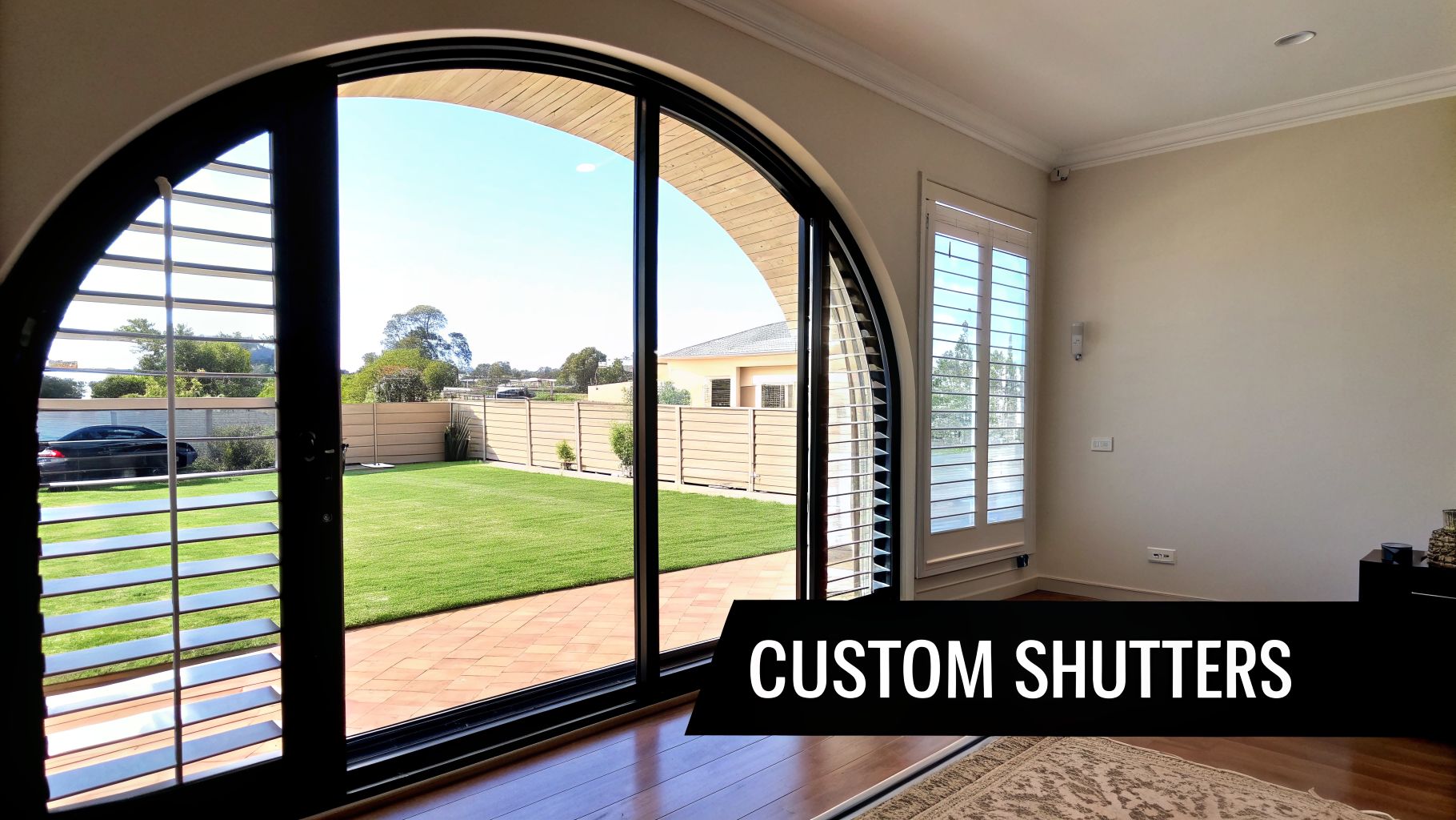 Interior view of a living room with an arched glass door and rectangular window featuring custom plantation shutters.