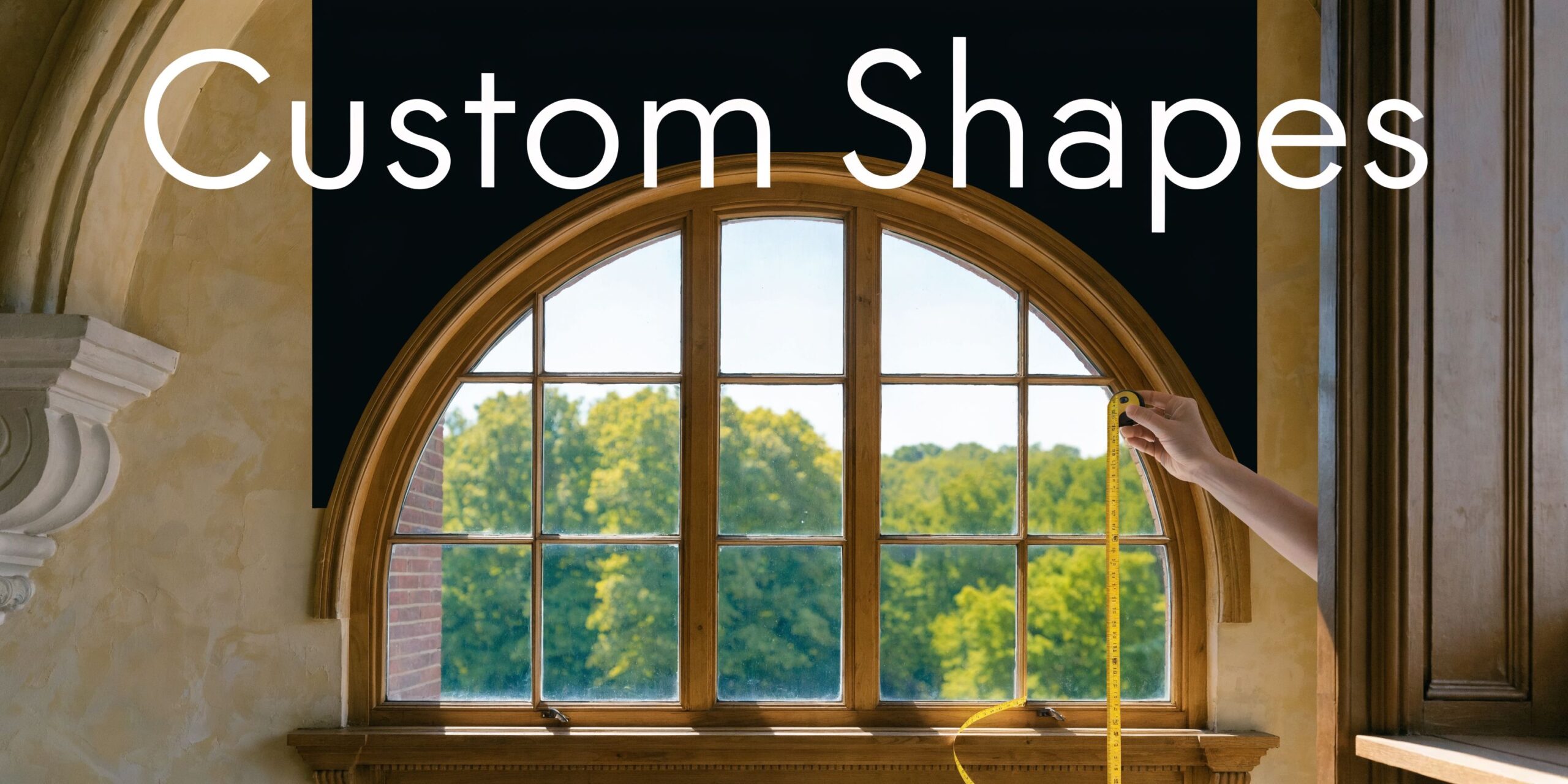 A person using a yellow tape measure to determine the dimensions of an arched wooden window frame.