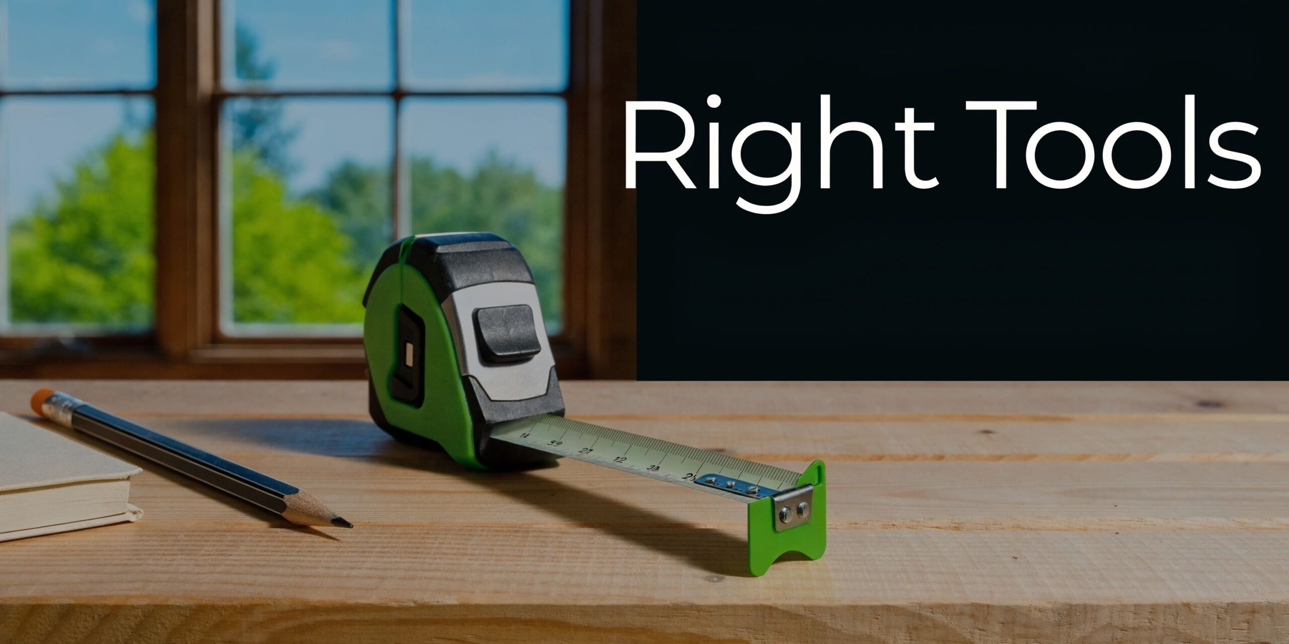 A tape measure and a pencil resting on a wooden surface in front of a window.